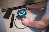 Person using an inspection camera to examine a hidden space beneath a surface.