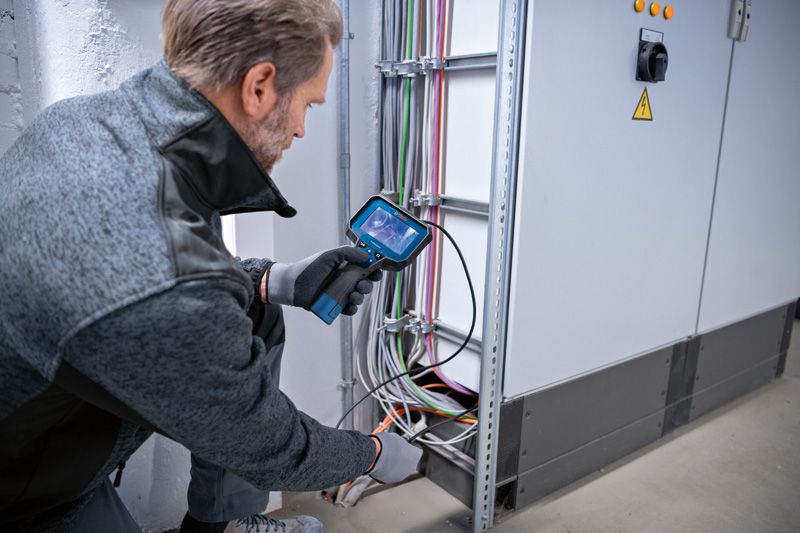 A person wearing safety equipment inspects electrical cables with an inspection camera.