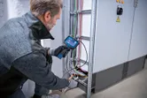 A person wearing safety equipment inspects electrical cables with an inspection camera.