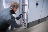 A person wearing safety equipment inspects electrical wiring with an inspection camera.