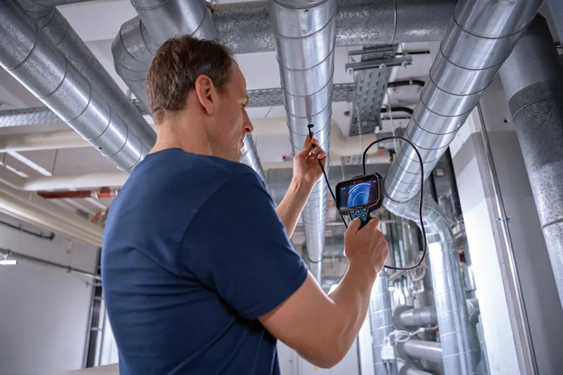 A person inspects ventilation ducts using an inspection camera.