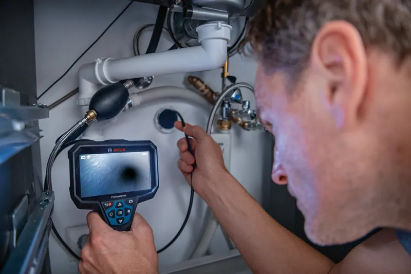 A person uses an inspection camera to examine plumbing connections under a sink.