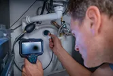 A person uses an inspection camera to examine plumbing connections under a sink.