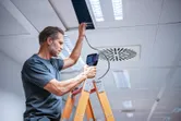 Person on a ladder inspects a ceiling with an inspection camera.