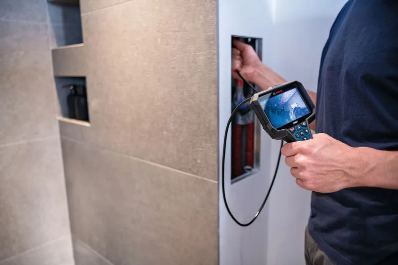 A person uses an inspection camera to examine wiring inside a wall.