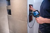 A person uses an inspection camera to examine wiring inside a wall.
