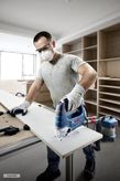 A person wearing safety equipment cuts wood with a jigsaw in a workshop.