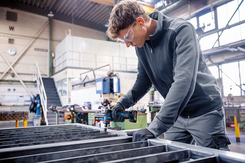 一名配戴安全設備的人員在金屬框架上使用旋轉研磨機。.