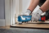 A person wearing safety equipment trims wood flooring with a cordless multi-tool.