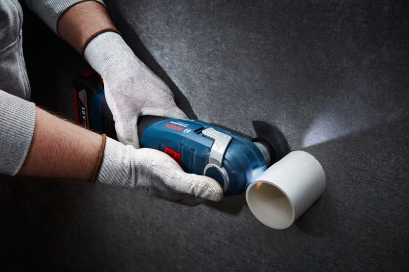A person wearing safety equipment cuts a plastic pipe with a cordless oscillating tool.