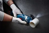 A person wearing safety equipment cuts a plastic pipe with a cordless oscillating tool.