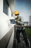 一名配戴安全設備的人員在鷹架上對建築物外部鑽孔。
