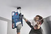 一名穿戴安全裝備的人員使用無線電錘在天花板上鑽孔。