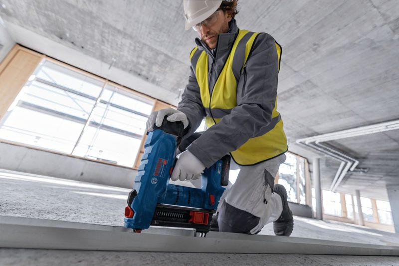 一名穿戴安全裝備的人員正在建築工地使用電動工具固定金屬框架。