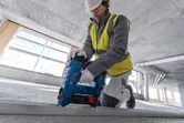 一名穿戴安全裝備的人員正在建築工地使用電動工具固定金屬框架。
