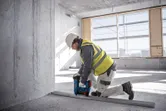 一名穿戴安全裝備的人員使用電動工具將金屬軌道固定在水泥地面上。