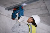 一名穿戴安全裝備的人員使用電動工具將金屬框架固定在天花板上。