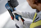 一名穿戴安全裝備的人員正在建築工地調整一台無線電動工具。