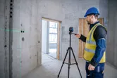一名穿戴安全裝備的人員正在建築工地調整架在三腳架上的雷射水平儀。