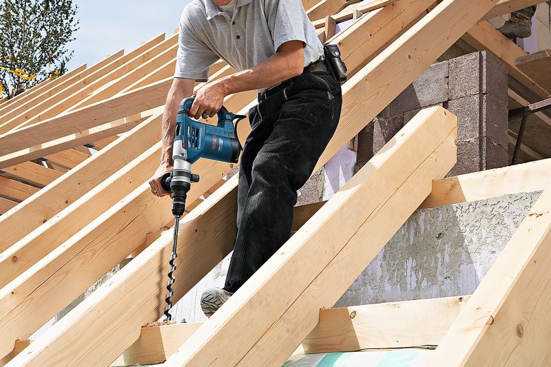 一名人員在屋頂結構的木樑上鑽孔，沒有配戴安全設備。.