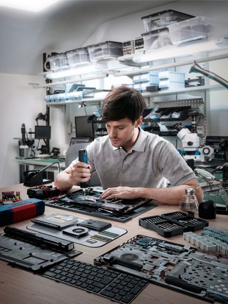 Person assembling electronic devices with a cordless screwdriver in a workshop.