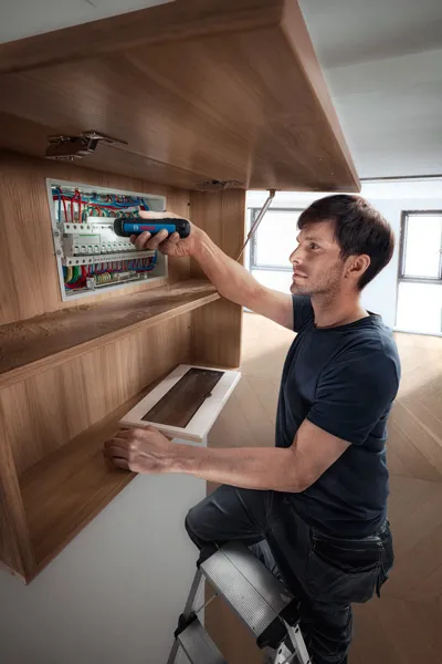 梯子上的人使用無線螺絲起子對配電盤進行操作。.