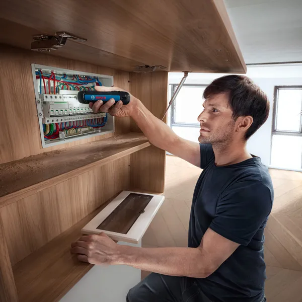 一個人使用無線螺絲起子固定配電盤中的電線。.