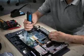 一個人在工作台上使用無線螺絲起子組裝筆記型電腦。.