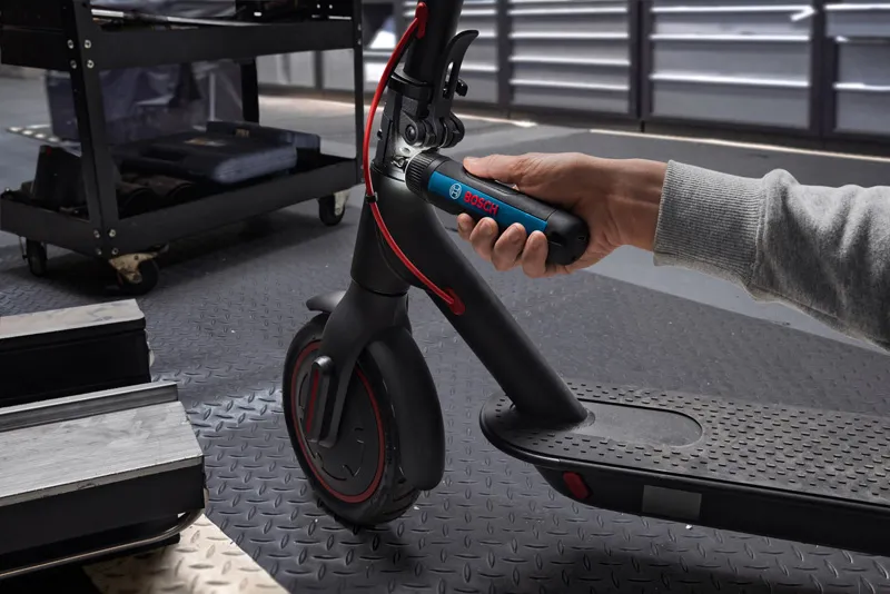 A person uses a cordless screwdriver to adjust the handlebar of an electric scooter.