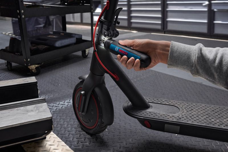 一個人用無線螺絲起子調整電動滑板車的車把。.