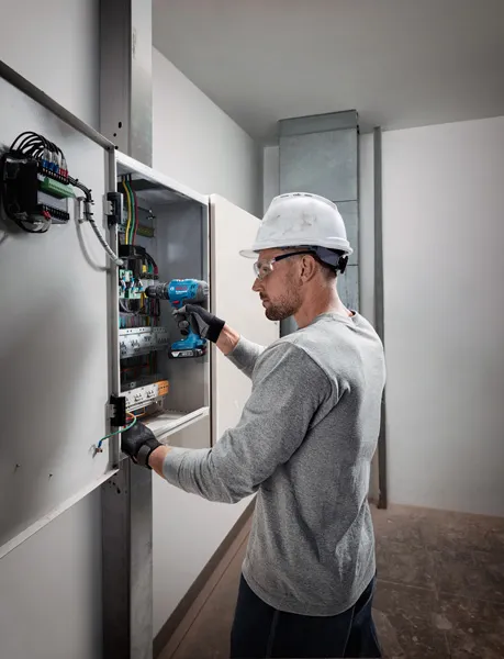 佩戴安全設備的人員使用無線電鑽在電氣面板上工作。.