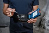 Person holds a compact LED work light with attached battery in an industrial setting.