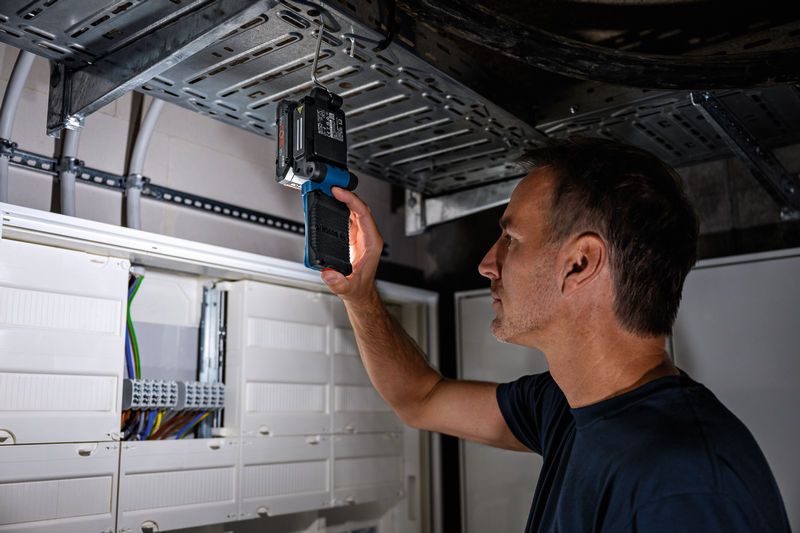 Person inspects metal cable tray with an electronic device near electrical panels.