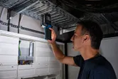 Person inspects metal cable tray with an electronic device near electrical panels.