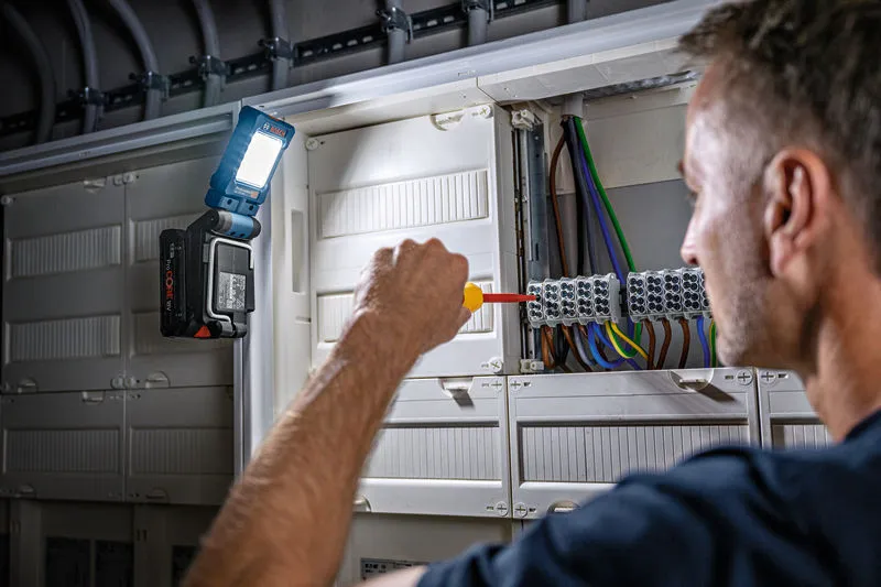 Person working on electrical panel with a flashlight illuminating the wiring.