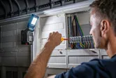 Person working on electrical panel with a flashlight illuminating the wiring.