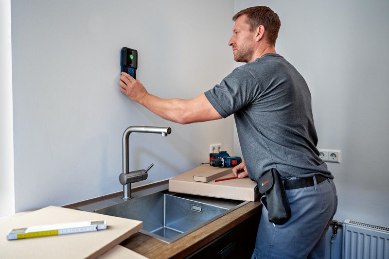 Person using a detector above a kitchen sink during a home improvement task.