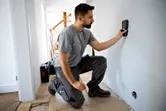 Person kneeling scans a wall with a detector in a residential space.