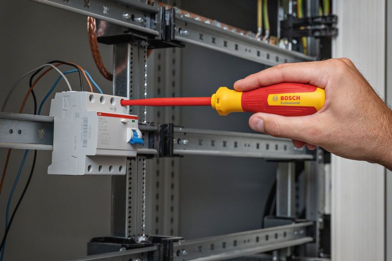 一個人用絕緣螺絲起子擰緊電氣面板上的接線端子螺絲。.