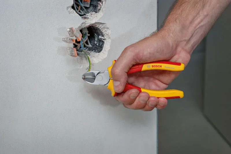 一個人用絕緣鉗子從電線盒中剪斷一根綠色電線。.