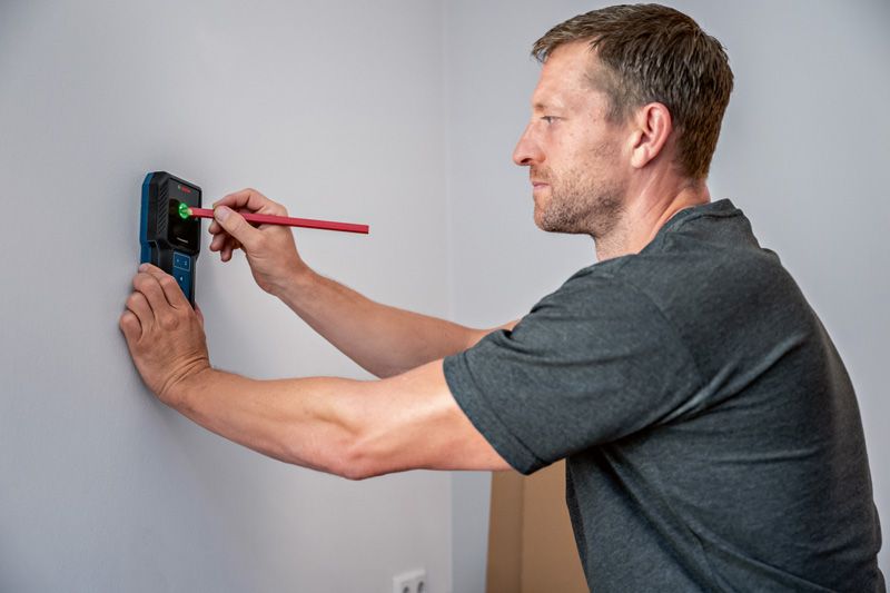 Person marking a wall while using an electronic detector.