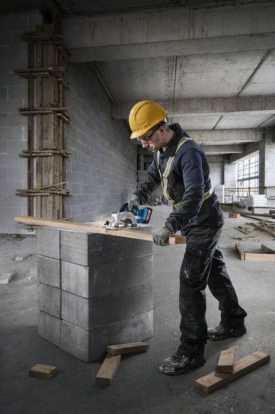 在建築工地上，一名配戴安全設備的人員正在用圓鋸切割木材。.
