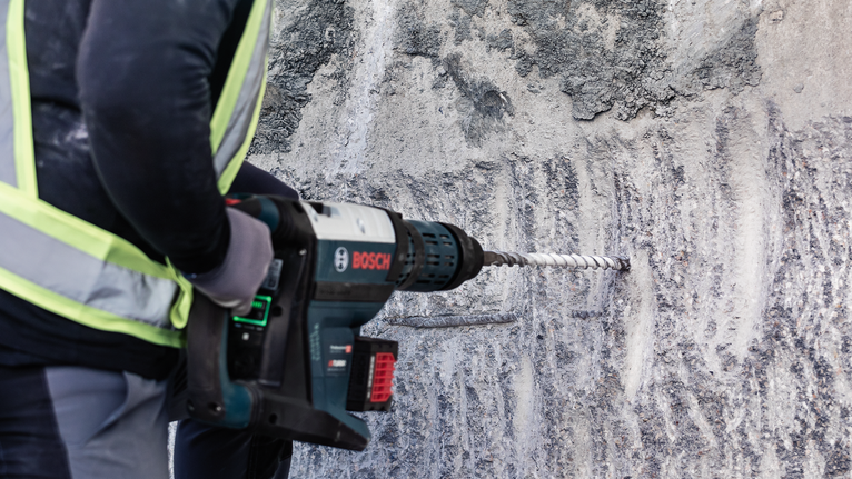 一名配戴安全設備的人員使用電動工具在混凝土牆上鑽孔。