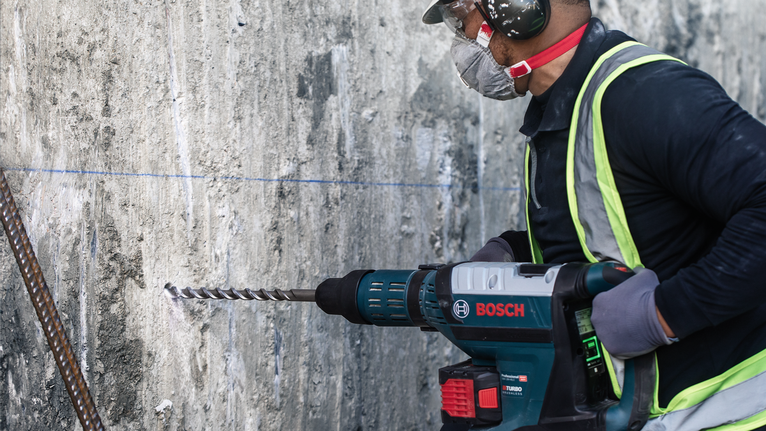 一名佩戴安全設備的人正在鑽入混凝土牆。