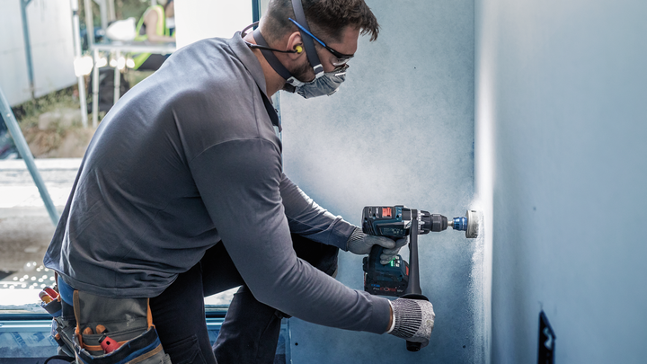 一名配戴安全設備的人員在幹牆上鑽了一個圓孔。