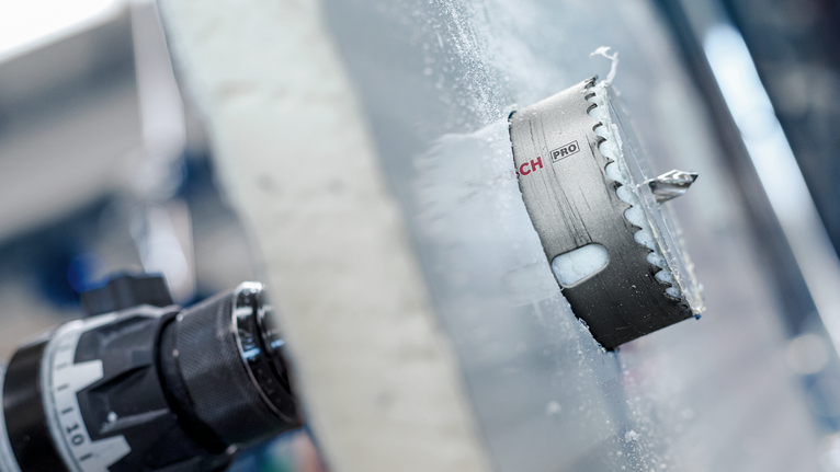 安裝在鑽頭上的孔鋸正在切割磨砂玻璃表面。