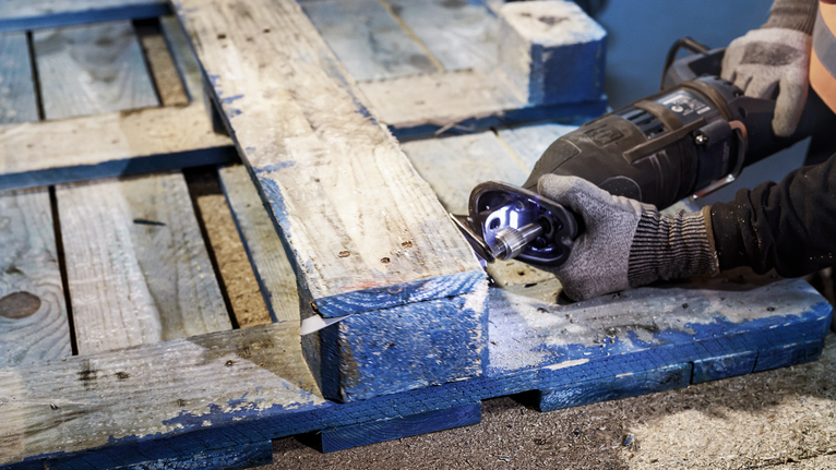 配戴安全設備的人員使用往復鋸切割木托盤。