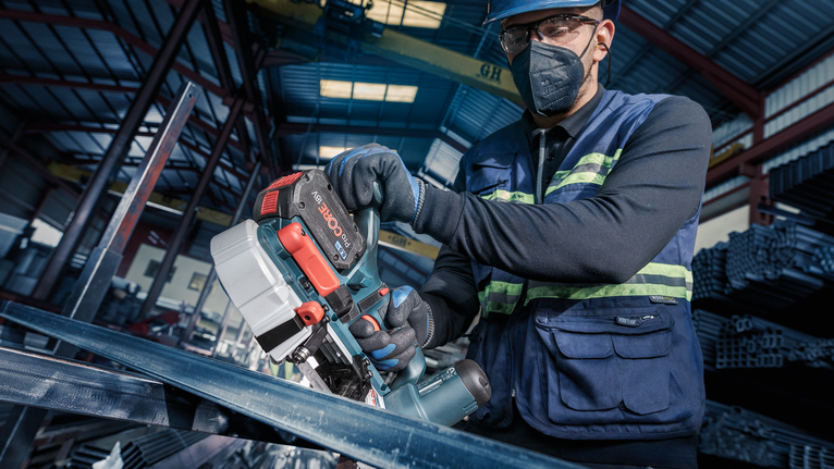 配戴安全設備的人員在工業環境中使用攜帶式電鋸切割金屬。