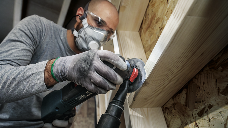 配戴安全設備的人員使用角磨機打磨木製框架。