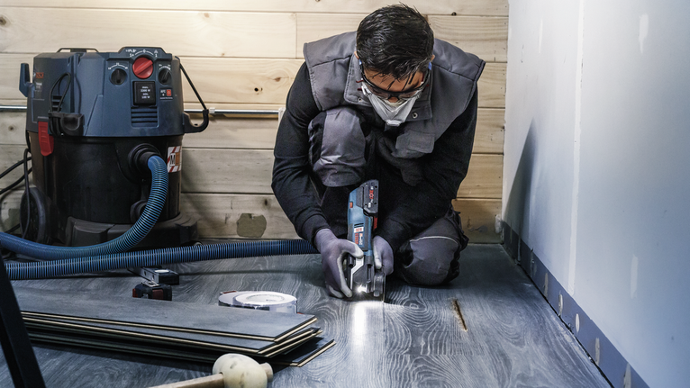 一名配戴安全設備的人員正在使用電動工具切割複合地板。